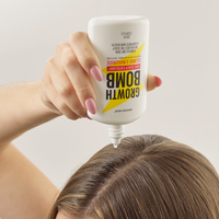 A hand with pink nails applies 100 ML’s AHA Scalp Exfoliant along the parting of brown hair, helping to gently remove buildup from the scalp.