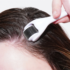 A person uses a Growth Bomb US Derma Roller for scalp care along the hairline. With fine needles and a sleek white handle, this tool enhances the precision of hair and micro-needling treatments.