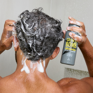 Shampoo and conditioner bottle in hands, with white foam on wet dark curly hair