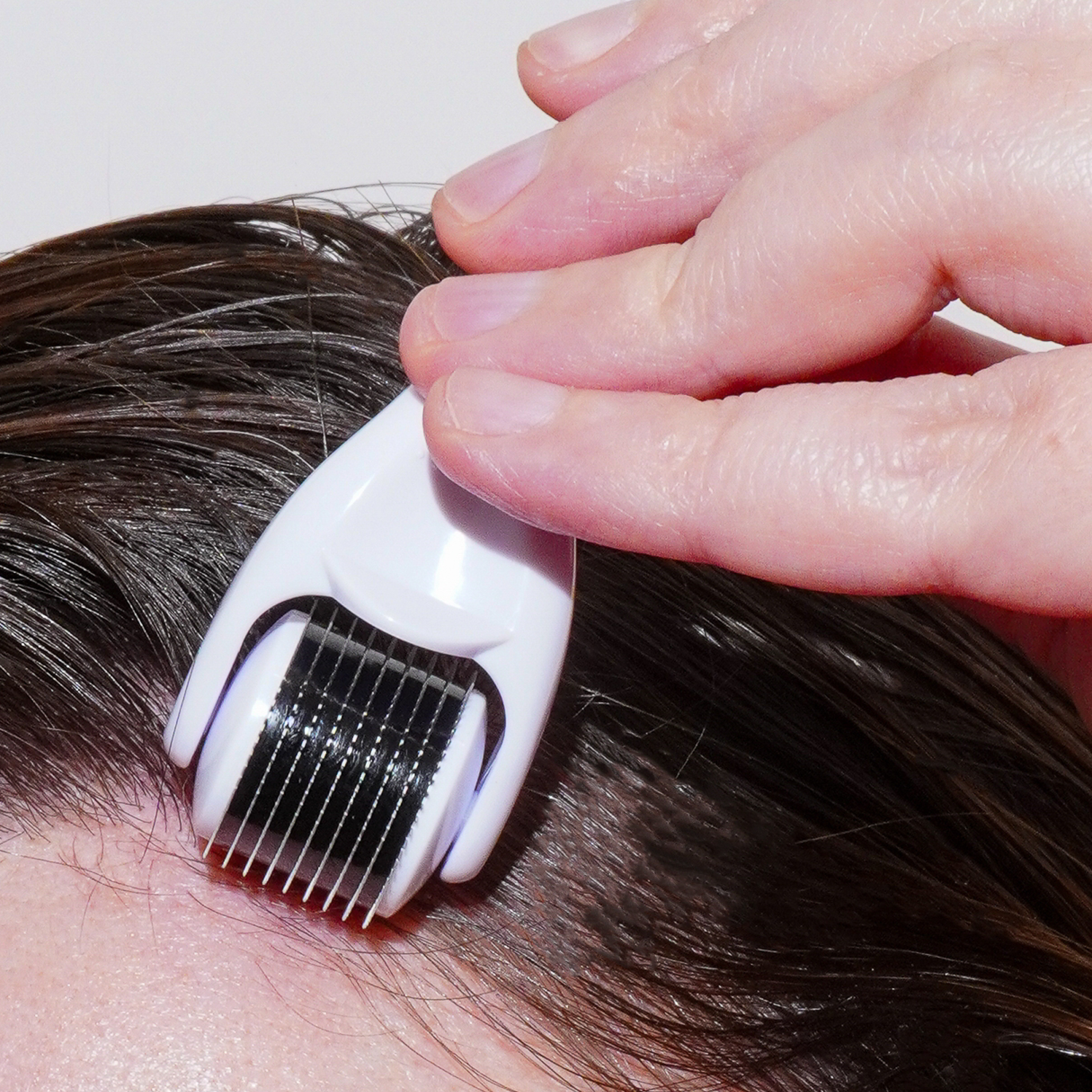 White derm roller comb pressed onto scalp with fingers