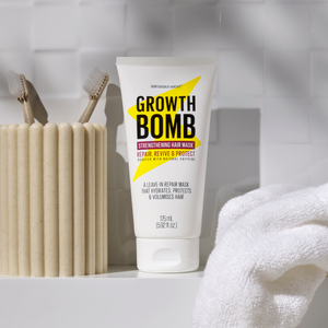 A Growth Bomb US Rescue, Restore & Hydrate Bundle sits on a bathroom shelf beside a textured toothbrush holder and two toothbrushes. To the right, a folded white towel complements the scene, enhancing the rescue remedy feel for your hair care routine.