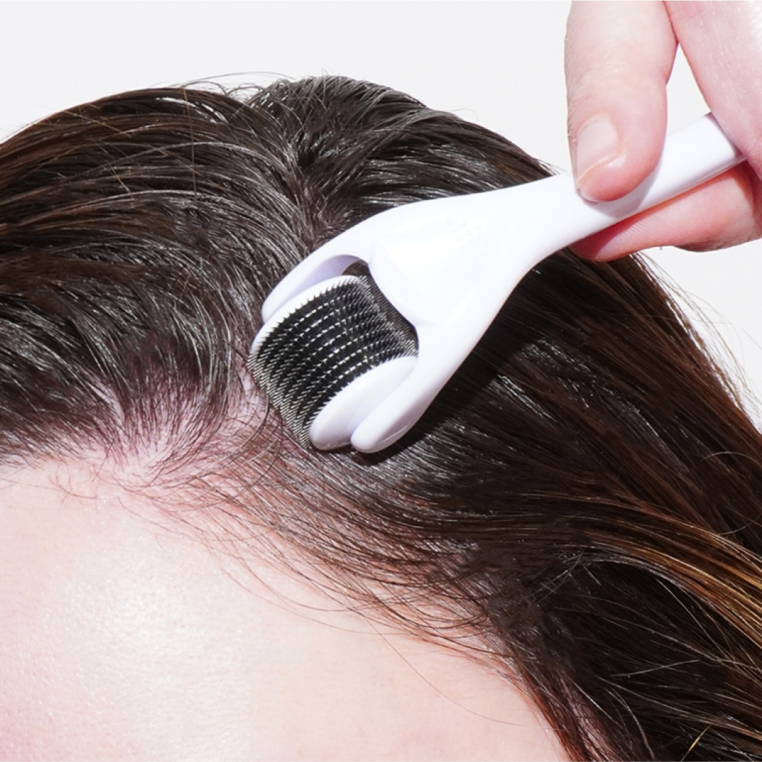 A person uses a Growth Bomb US Derma Roller for scalp care along the hairline. With fine needles and a sleek white handle, this tool enhances the precision of hair and micro-needling treatments.