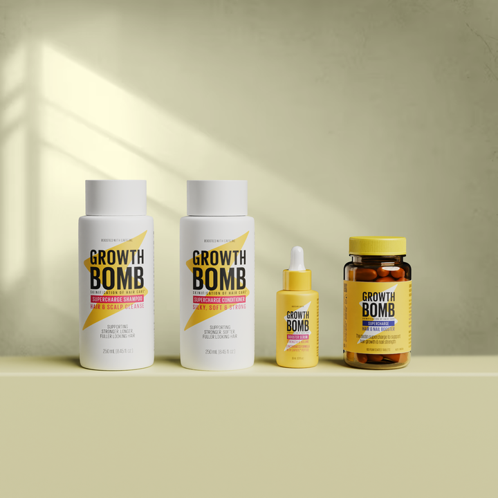 Four hair care products from the Hair Growth Support Bundle by Growth Bomb US are on a beige surface: two white bottles, a small yellow dropper bottle labeled Booster Serum, and a brown jar with a yellow lid against a textured background.