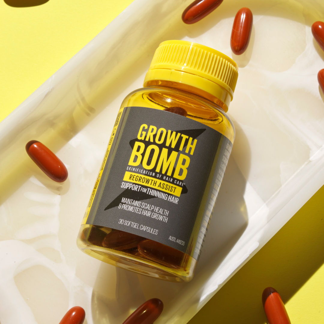 A bottle of Regrowth Assist Support for Thinning Hair Supplement by Growth Bomb US rests on a white tray surrounded by brown capsules. Its label promises to enhance hair thickness, while a vibrant yellow background energetically highlights its focus on revitalizing hair growth.