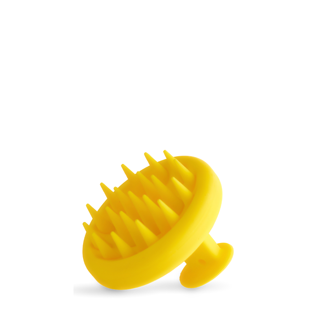 The Growth Bomb Silicone Scalp Brush is yellow with a handle, featuring soft spikes for hair and scalp exfoliation, shown on a white background.