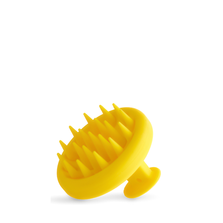 The Growth Bomb Silicone Scalp Brush is yellow with a handle, featuring soft spikes for hair and scalp exfoliation, shown on a white background.